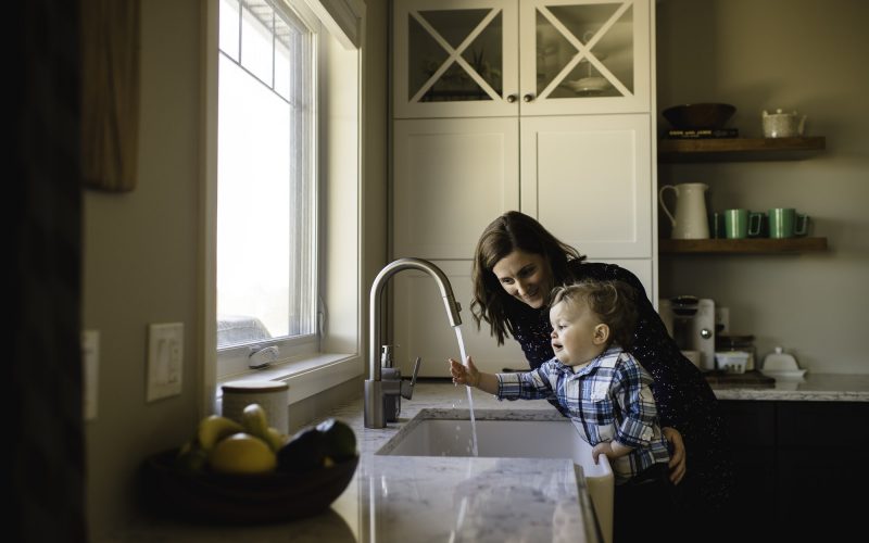 Mother helping toddler son wash hands at kitchen sink